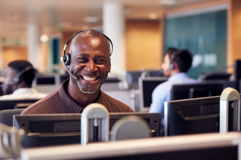 Portrait Of Mature Businessman Wearing Telephone Headset Working In Customer Services Department